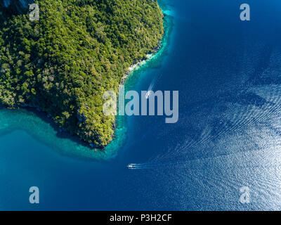 Aerial drone view down onto boats over a tropical coral reef surrounded by mountains and jungle Stock Photo