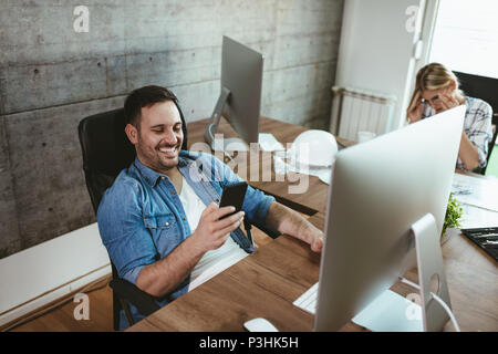 Young handsome successful freelance entrepreneur having fun and working on computer at the office. He is surfing on social media. Stock Photo