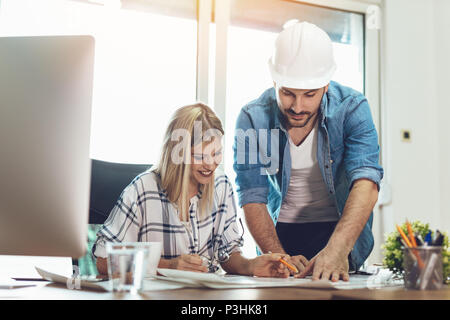 Young worried architect colleagues talking and analyzing blueprints while working on a new project at the office. Stock Photo