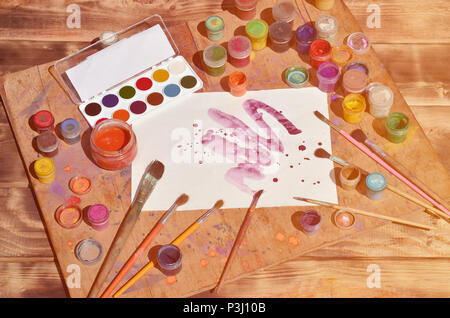 Background image showing interest in watercolor painting and art. A painted sheet of paper, surrounded by brushes, jars of watercolor paint and gouach Stock Photo