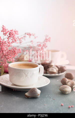 Chocolate sweets in the form of cockleshells and two cups of fragrant coffee. Romantic breakfast. Light colors. Pink flowers. Free space for text. copy space. Stock Photo
