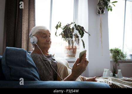 Senior woman listening to music on headphones while using mobile phone Stock Photo