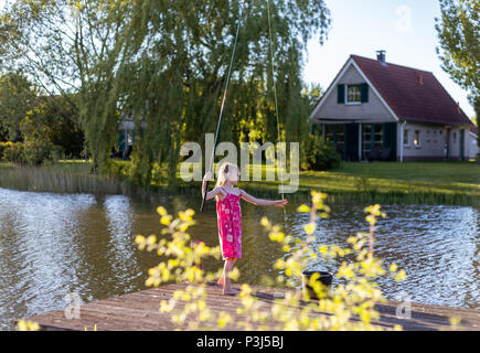 A 7 year old girl stands with fishing rod on the jetty and looks for the bait Stock Photo