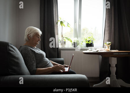 Senior woman using laptop in living room Stock Photo