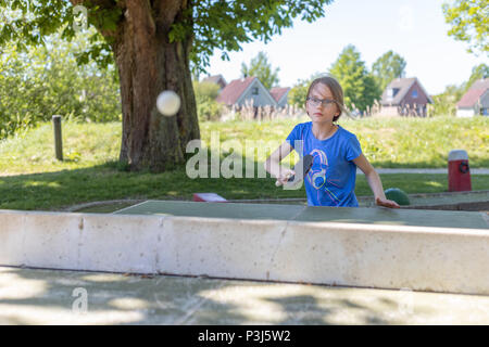 A 9 year old girl plays table tennis on an outside ping-pong table. She is playing the a smash Stock Photo