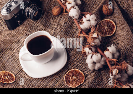 Coffee in a white cup with dry cotton on burlap and retro camera Stock Photo