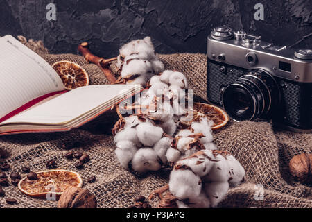 Old film camera on a table with burlap dry cotton on a branch with a notebook coffee beans and dry orange slices Stock Photo