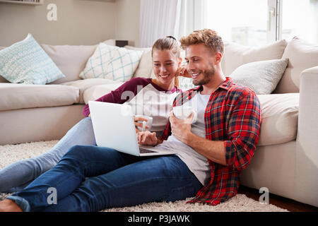 Young white couple sitting on the floor at home using laptop Stock Photo