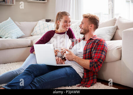 Young white couple sitting on the floor at home using laptop Stock Photo