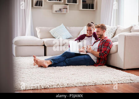 Young white couple sitting on the floor at home using laptop Stock Photo