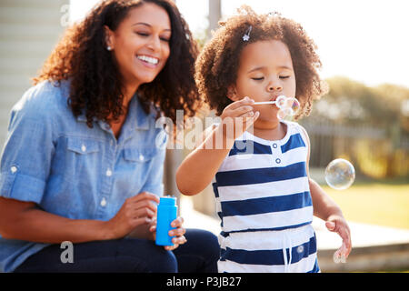 Young mixed race mother and daughter blowing bubbles outside Stock Photo