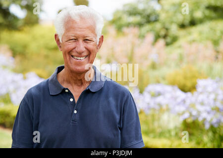 Portrait Of Senior Man Enjoying Walk By Flower Beds In Park Stock Photo