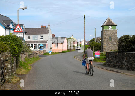 A man cycling on his bike past the Clock House Cafe and clock tower in Marloes village in Pembrokeshire West Wales, UK  KATHY DEWITT Stock Photo