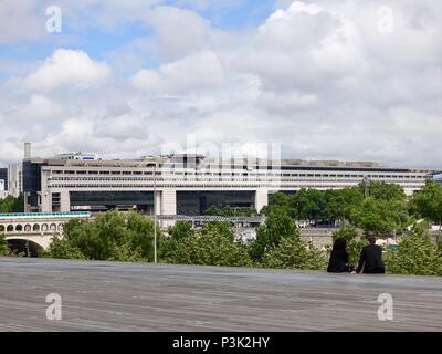Couple sit in front of the library overlooking the Seine River and the Pont de Bercy on a warm, June day, Paris, France Stock Photo