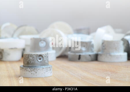 Several plastic nozzles from a paint sprayer that lie on a wooden surface against a gray wall background. The caps are smeared in chrome paint. The co Stock Photo