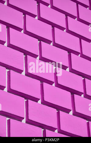 Decorative concrete wall with a relief similar to a large brick masonry painted in bright pink paint Stock Photo