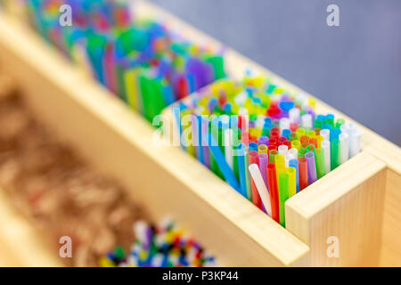 Bunch of colorful plastic sipping straws in wooden box at cafe counter. Drinks decoration and accessories. Bright multicolored background. Stock Photo