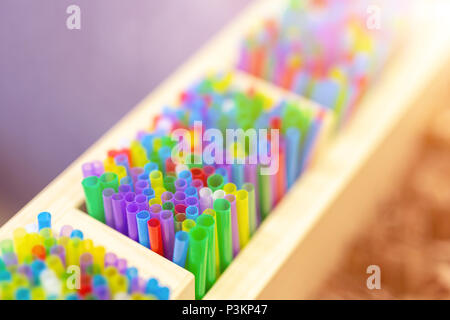 Bunch of colorful plastic sipping straws in wooden box at cafe counter. Drinks decoration and accessories. Bright multicolored background. Stock Photo