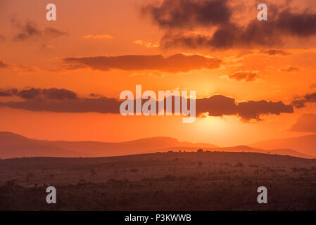 The sun glows behind purple clouds in an intense orange red sky at sunset over Blyde River Canyon hills in Mpumalanga, South Africa Stock Photo