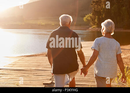 Romantic Senior Couple Walking On Wooden Jetty By Lake Stock Photo