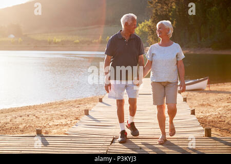Romantic Senior Couple Walking On Wooden Jetty By Lake Stock Photo