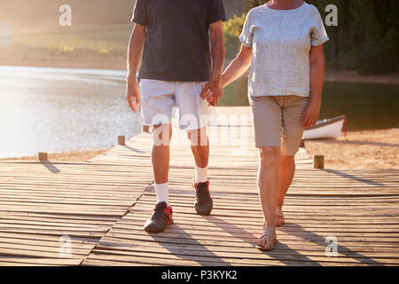 Close Up Of Romantic Senior Couple Walking On Jetty By Lake Stock Photo