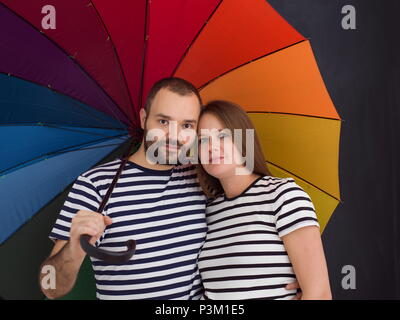 portrait of husband and pregnant wife posing with colorful umbrella in front of black chalk drawing board Stock Photo