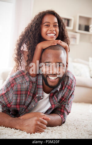 Portrait Of Daughter Lying On Fathers Back In Lounge Stock Photo