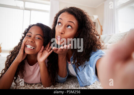 Mother And Daughter Lying On Rug And Posing For Selfie At Home Stock Photo