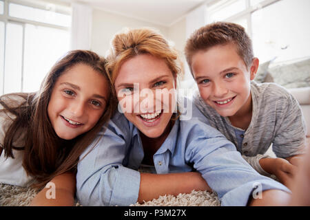 Mother And Children Lying On Rug And Posing For Selfie At Home Stock Photo