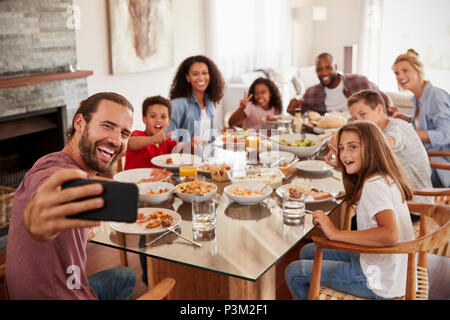 Two Families Taking Selfie As They Enjoy Meal At Home Together Stock Photo