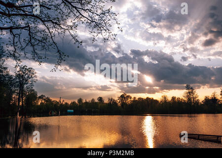 Sun shines between the heavy rains of the rain clouds over the flooded field in the park. Landscape, sunset Stock Photo