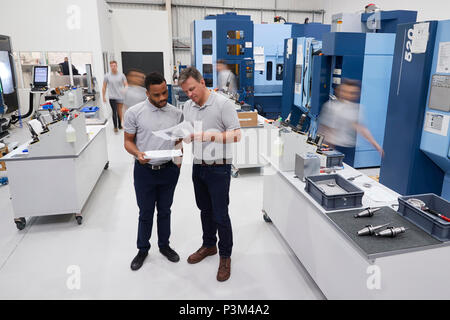 Engineers Meeting On Factory Floor Of Busy Engineering Workshop Stock Photo