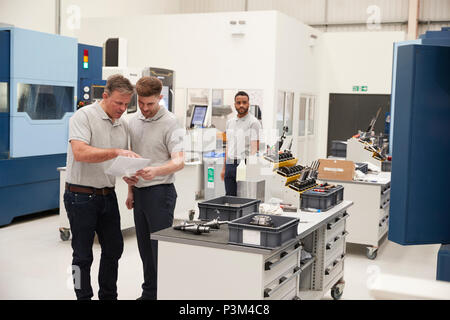 Engineer And Apprentice Meet On Floor Of Engineering Workshop Stock Photo