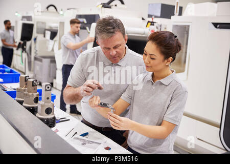 Engineer And Female Apprentice Measuring Components In Factory Stock Photo