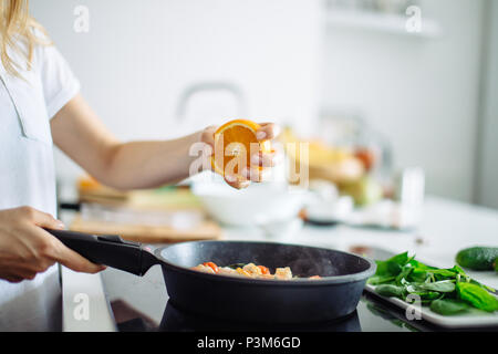Young housewife cooking in kitchen, squeezing the orange on the frying pan Stock Photo
