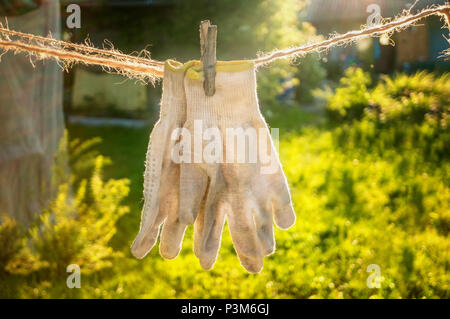 Old working textile gloves are dried on the twine after washing. Hand protection. Stock Photo