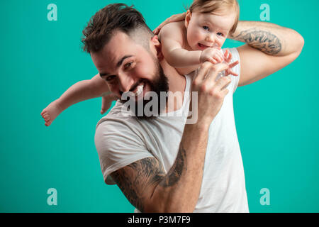 Playful father carrying his smiling infant child on neck over blue background