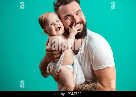 Playful father carrying his smiling infant child on neck over blue background