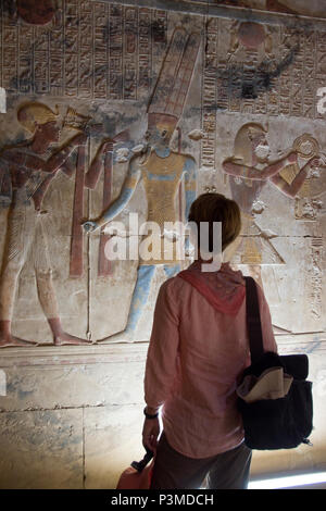 A tourist views colorfully painted bas relief stone carvings depict Pharaoh and Egyptian gods inside the Temple of Seti I, Abydos, Egypt. Stock Photo