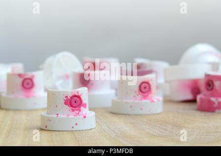 Several plastic nozzles from a paint sprayer that lie on a wooden surface against a gray wall background. The caps are smeared in pink paint. The conc Stock Photo