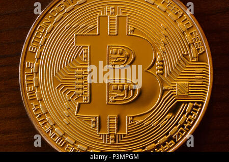 One new golden physical bitcoin is lies on dark wooden backgound, close up. High resolution photo. Cryptocurrency mining concept Stock Photo