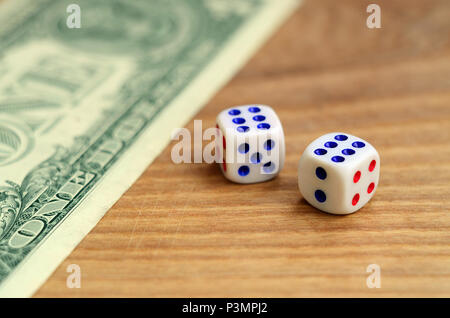 White dice are next to a dollar bill of US dollars on a wooden background. The concept of gambling with rates in monetary units Stock Photo