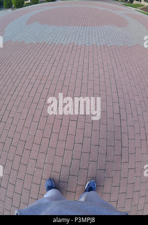 Men's legs in sports pants and sneakers stand on a large area of modern paving stones Stock Photo