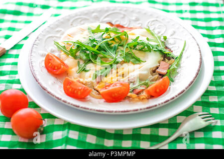 Fried eggs with fresh arugula and tomatoes cherry on wtite plate. Breakfast Stock Photo