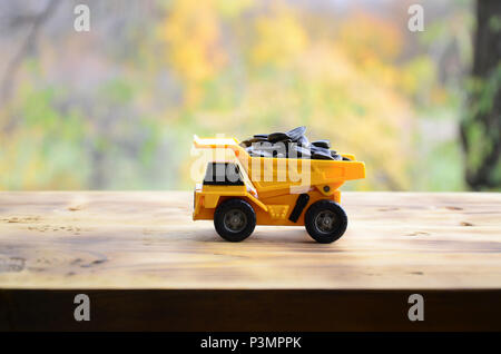 A small yellow toy truck is loaded with sunflower seeds. A car on a wooden surface against a background of autumn forest. Extraction and transportatio Stock Photo