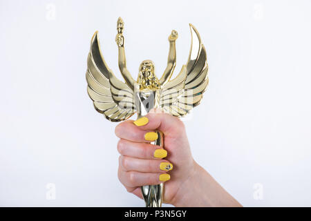 Golden Angel statue with torch and opened wings in female hand with yellow manicure nails isolated on white background. Close up, studio shoot Stock Photo