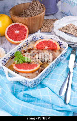 Baked chicken thighs with pink grapefruit in beautiful ceramic dishes with a blue pattern, basil. A blue kitchen towel. Lunch for the family Stock Photo