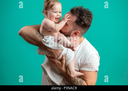 Playful father carrying his smiling infant child on neck over blue background