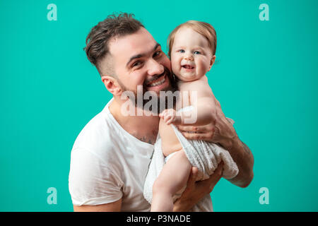 Playful father carrying his smiling infant child on neck over blue background